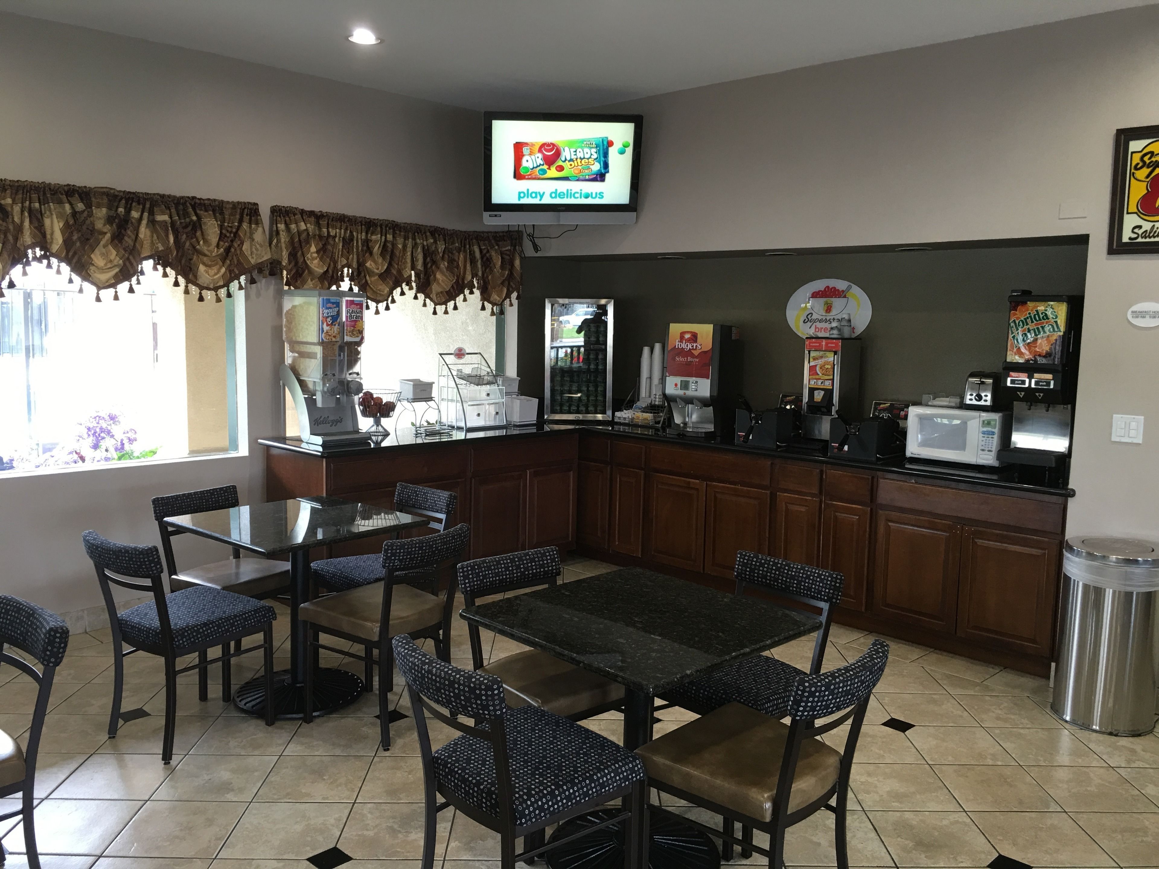 A restaurant with a counter, seating area, and a television displaying an advertisement.