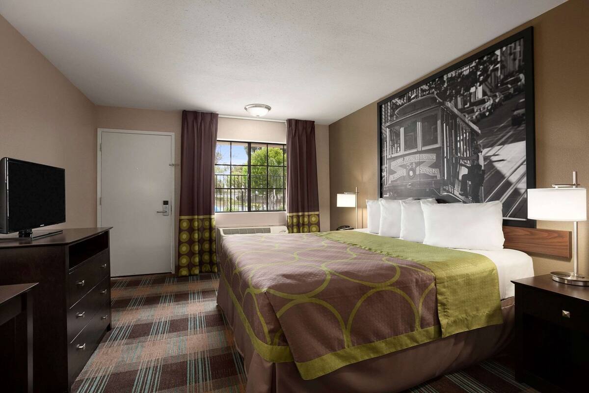 A hotel room with a bed, a TV, a desk, a chair, a lamp, and a window with curtains.