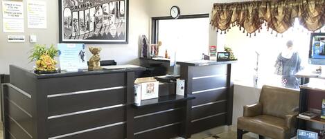 A reception area with a dark wooden desk, a clock, and a framed picture of a cityscape.