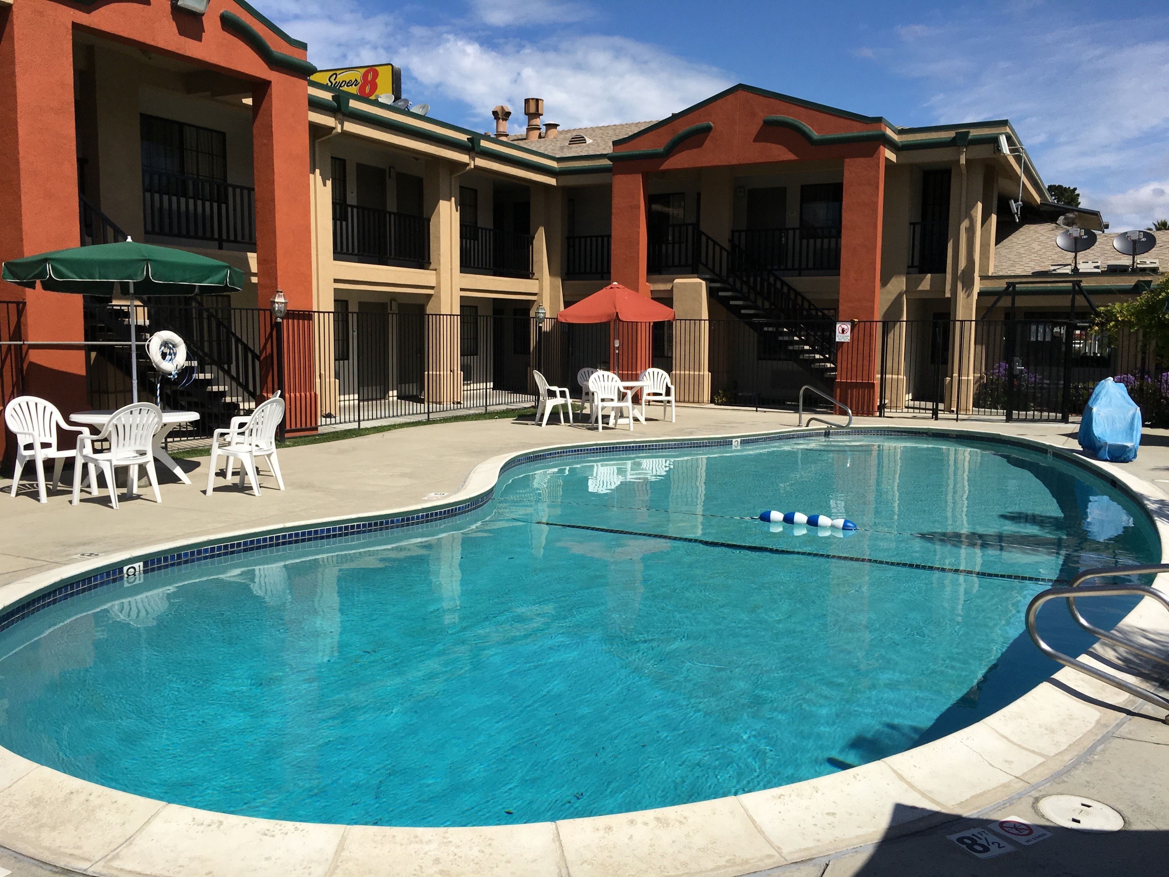 A swimming pool with white lounge chairs and umbrellas, a covered patio area, and a building with balconies.