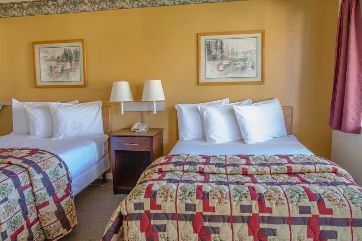 A hotel room with two beds, each with a different patterned bedspread, a nightstand with a lamp, and two framed pictures on the wall.