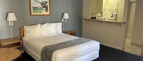 Habitación de hotel con cama, dos mesitas de noche, una mesa redonda, una silla, un cuadro, un espejo y baño a la vista a través de una puerta abierta.