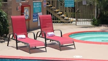Zona de piscina con dos sillones rojos, un cartel de capacidad de la piscina y un portón con un aviso que indica que no se permite el acceso a menores de 18 años.
