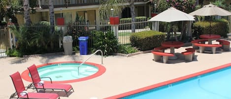 A swimming pool with lounge chairs and tables, surrounded by a fence and greenery.