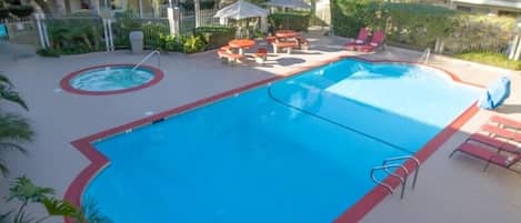 Piscina com borda vermelha, cercada por espreguiçadeiras e mesas, e uma banheira de hidromassagem no centro.