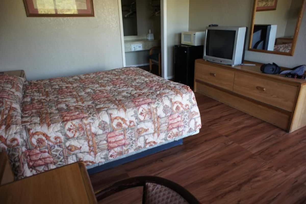 A bedroom with a bed, a dresser, a television, and a mirror.