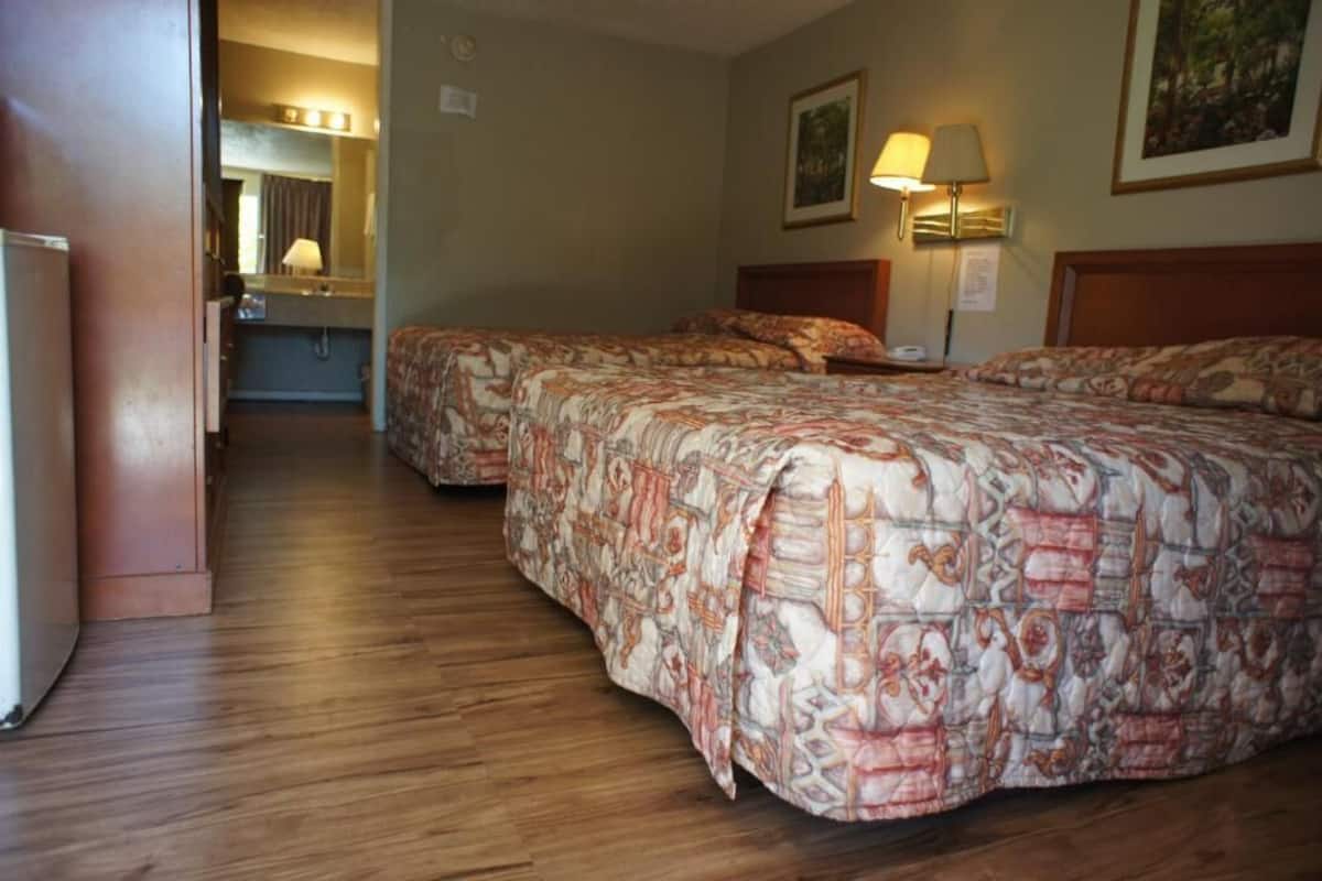 A hotel room with two beds, a wooden floor, a bathroom with a mirror, and a painting on the wall.