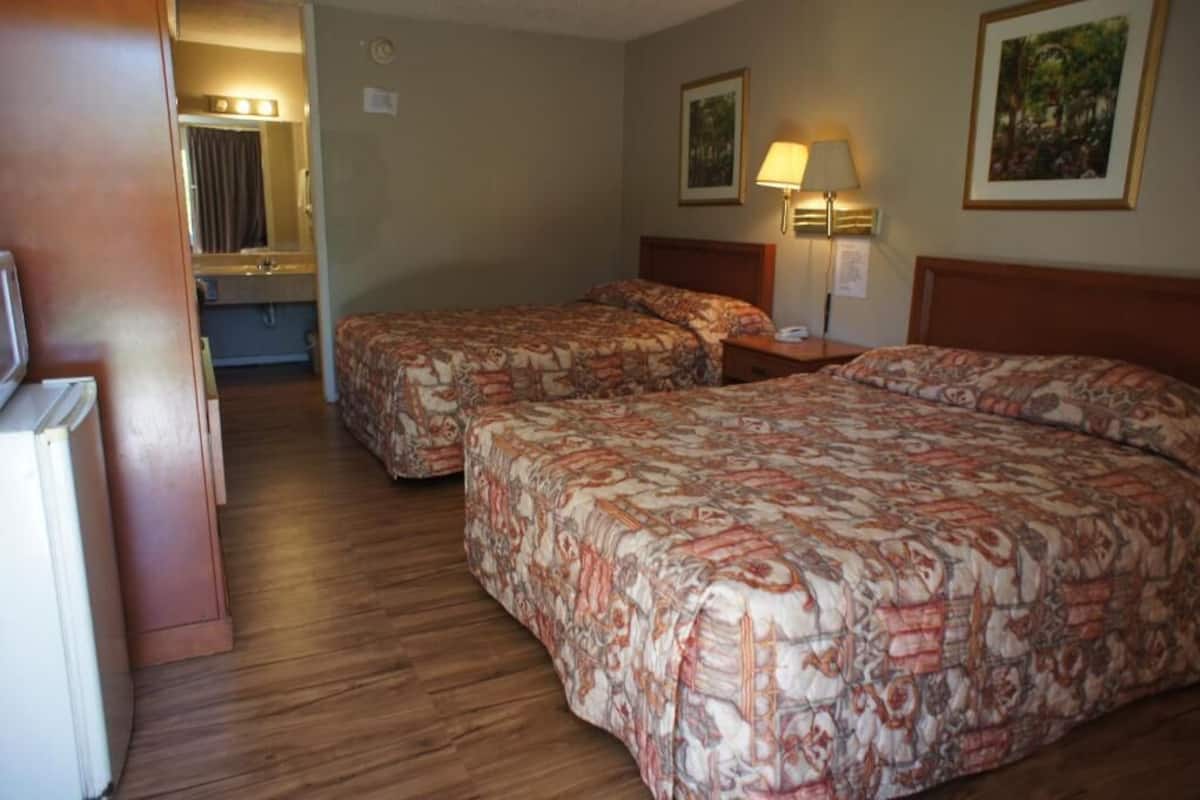 A hotel room with two beds, a bathroom, and a small desk with a lamp.