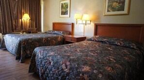 A hotel room with two beds, a chair, a lamp, and wall art.