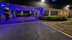 Entrada de hotel con zona de estacionamiento techada, un letrero que dice 'Hotel Away from Home' y un camino bien iluminado hacia la entrada.