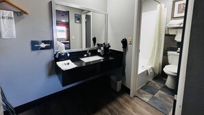 Un baño moderno con lavamanos negro, espejo y zona de ducha visible a través de una puerta abierta.