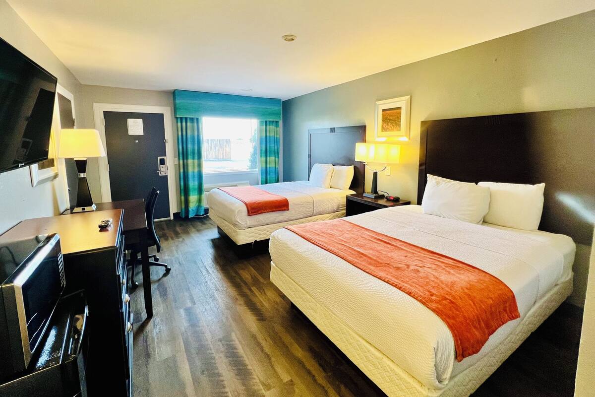 A hotel room with two beds, a desk, a chair, and a TV.