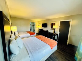 A hotel room with two beds, a desk, a chair, a TV, and a door.