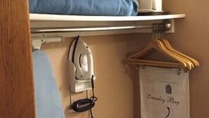 A bedroom with a bunk bed, an ironing board, and a hanging laundry bag. - Americas Best Value Inn York (York)