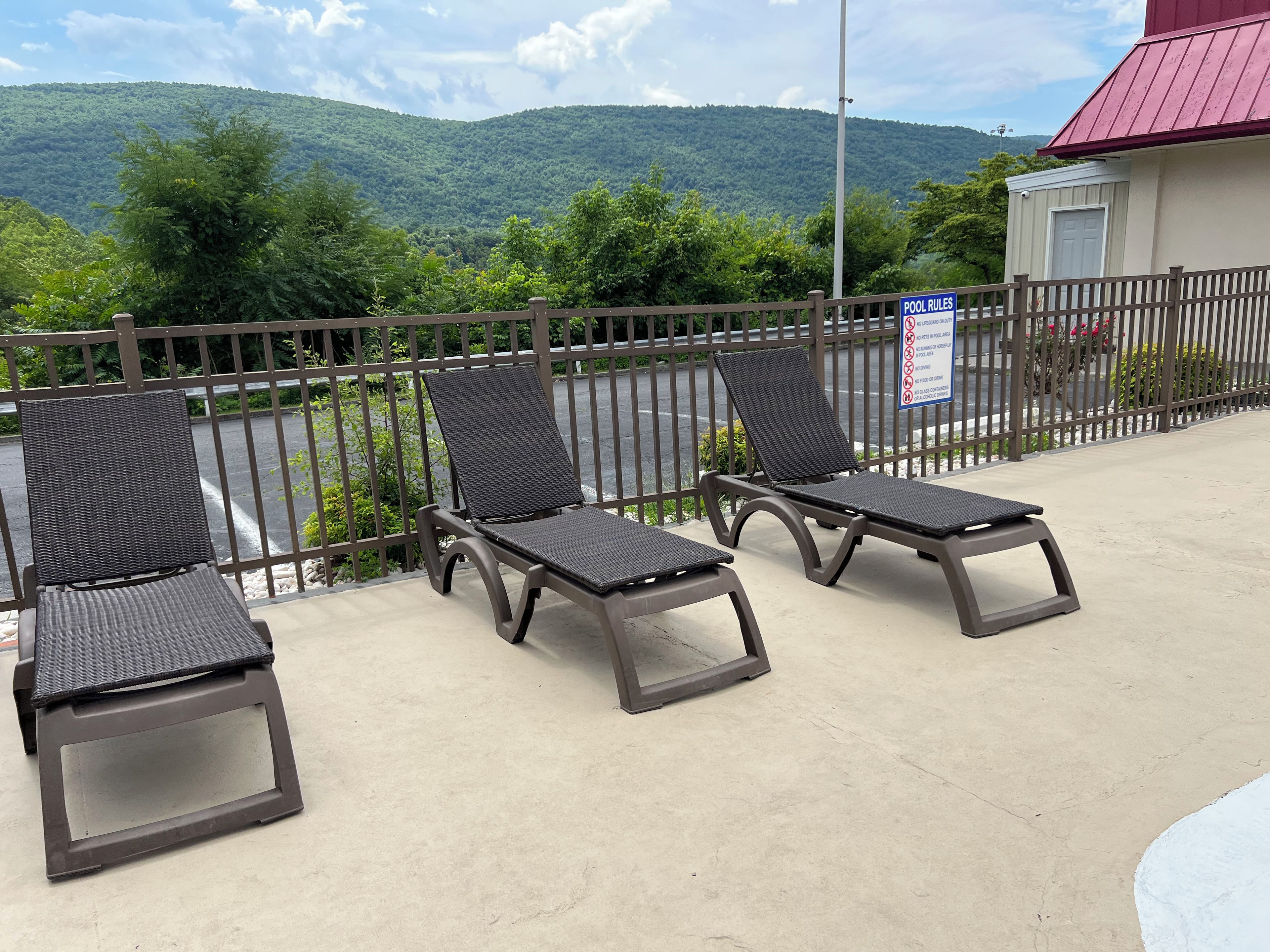 Un espace aménagé au bord de la piscine, avec trois chaises longues et un panneau indiquant les règles d’utilisation de la piscine.