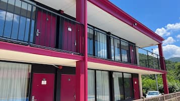 A two-story building with a red exterior, balconies with black railings, and a pool area visible through a glass door.