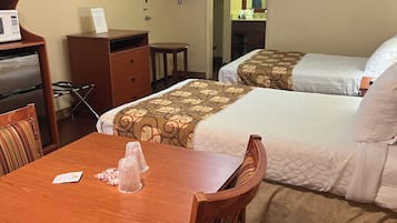 Habitación de hotel con una mesa de madera, dos camas, un ventilador de techo, un televisor y un microondas.