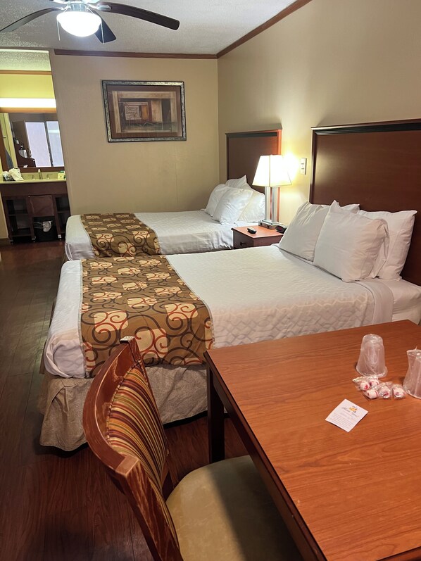A hotel room with two beds, a wooden desk, a chair, a desk lamp, and a framed picture on the wall.
