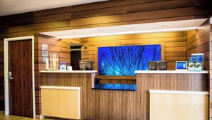 Un'area reception di un hotel dall'arredamento in legno, con un tappetino con la scritta 'Benvenuti' e uno schermo digitale che mostra una vista del cielo notturno.