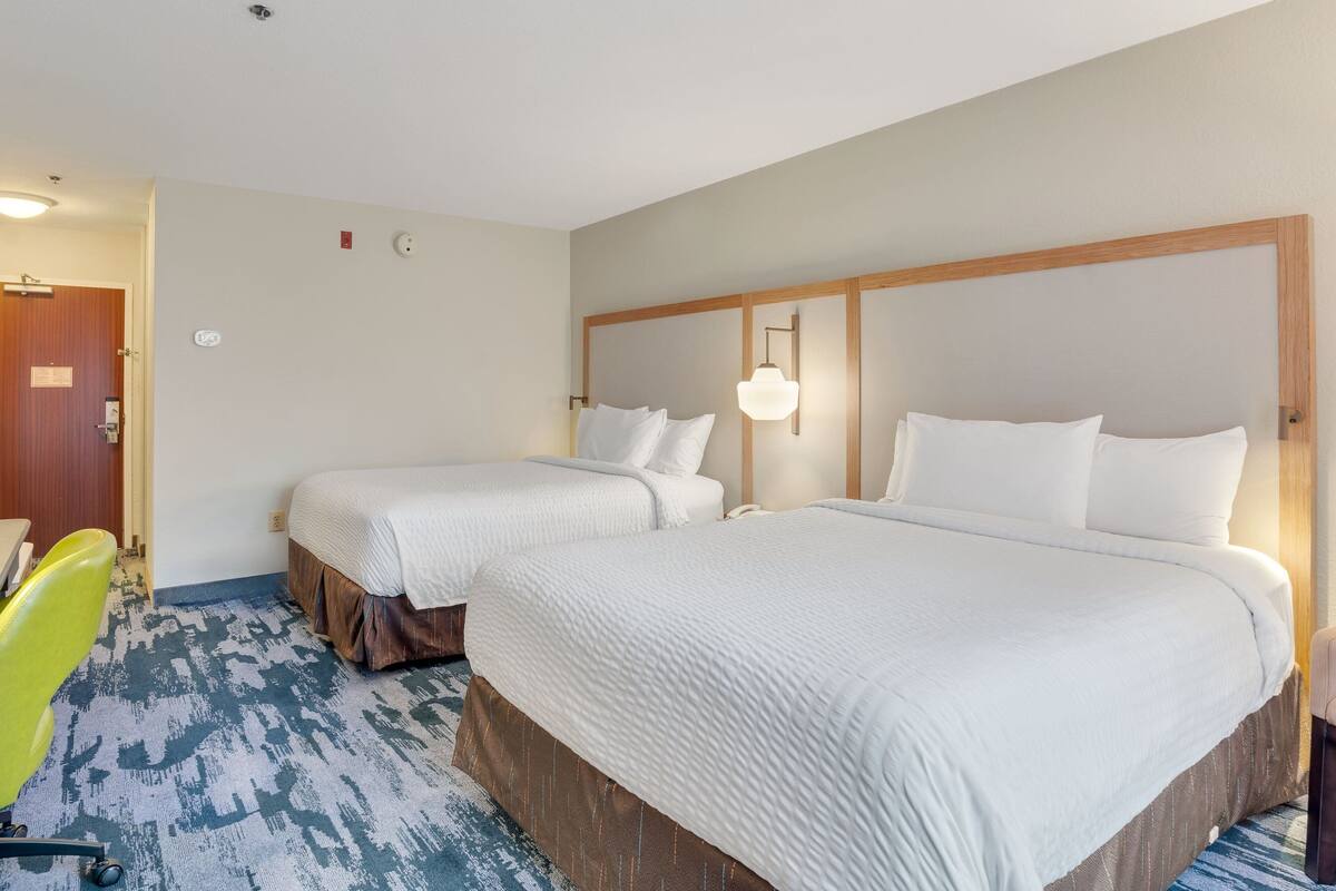 A hotel room with two beds, a desk, and a chair.