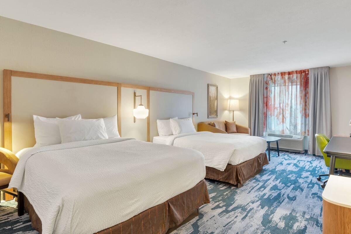 A hotel room with two beds, a desk, a chair, and a window with curtains.