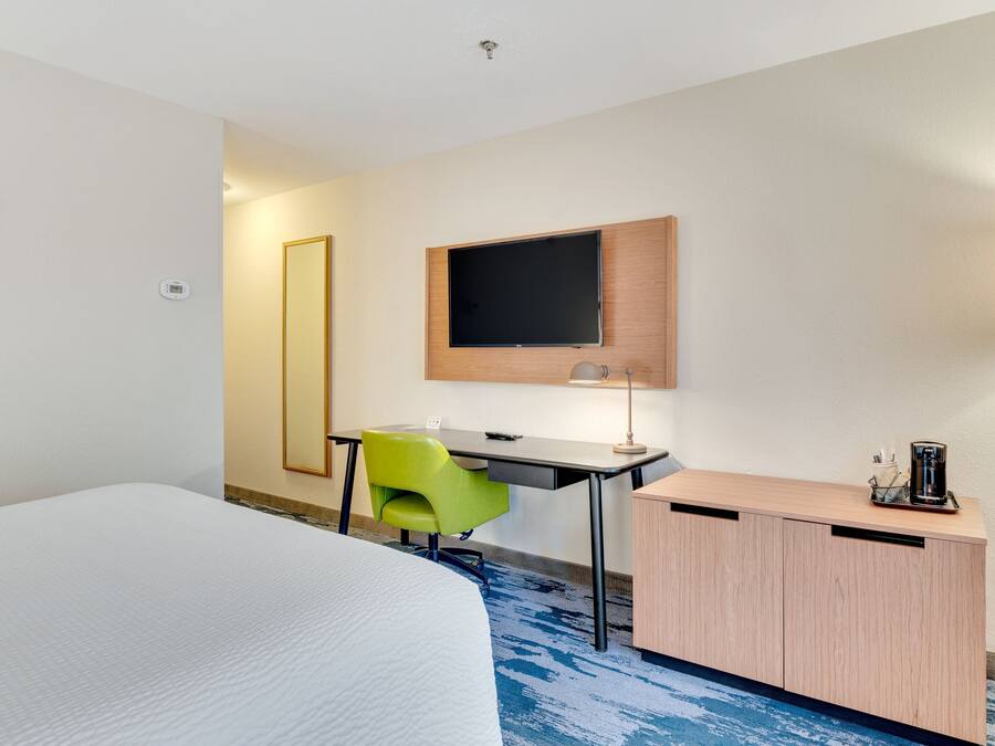 Una camera d'albergo con un letto, una scrivania, una sedia, una TV e un piccolo armadietto.