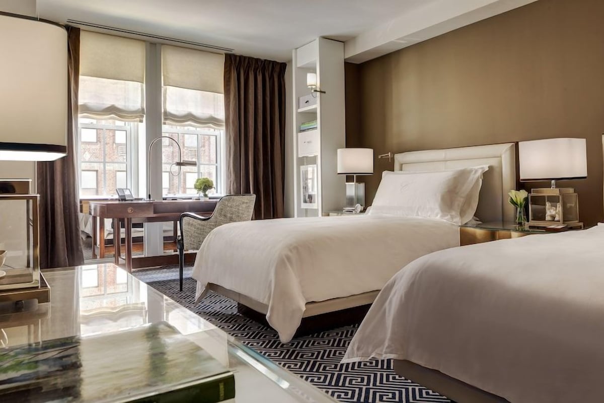A hotel room with two beds, a desk, a chair, and a large window with curtains.