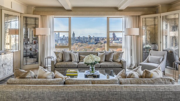 A spacious living room with a large window offering a city view, a comfortable sofa, a coffee table, and a side table with a lamp. - The Carlyle, A Rosewood Hotel (New York)