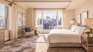 A modern hotel room with a large bed, a view of a city skyline, and a cityscape visible through the window. - The Carlyle, A Rosewood Hotel (New York)