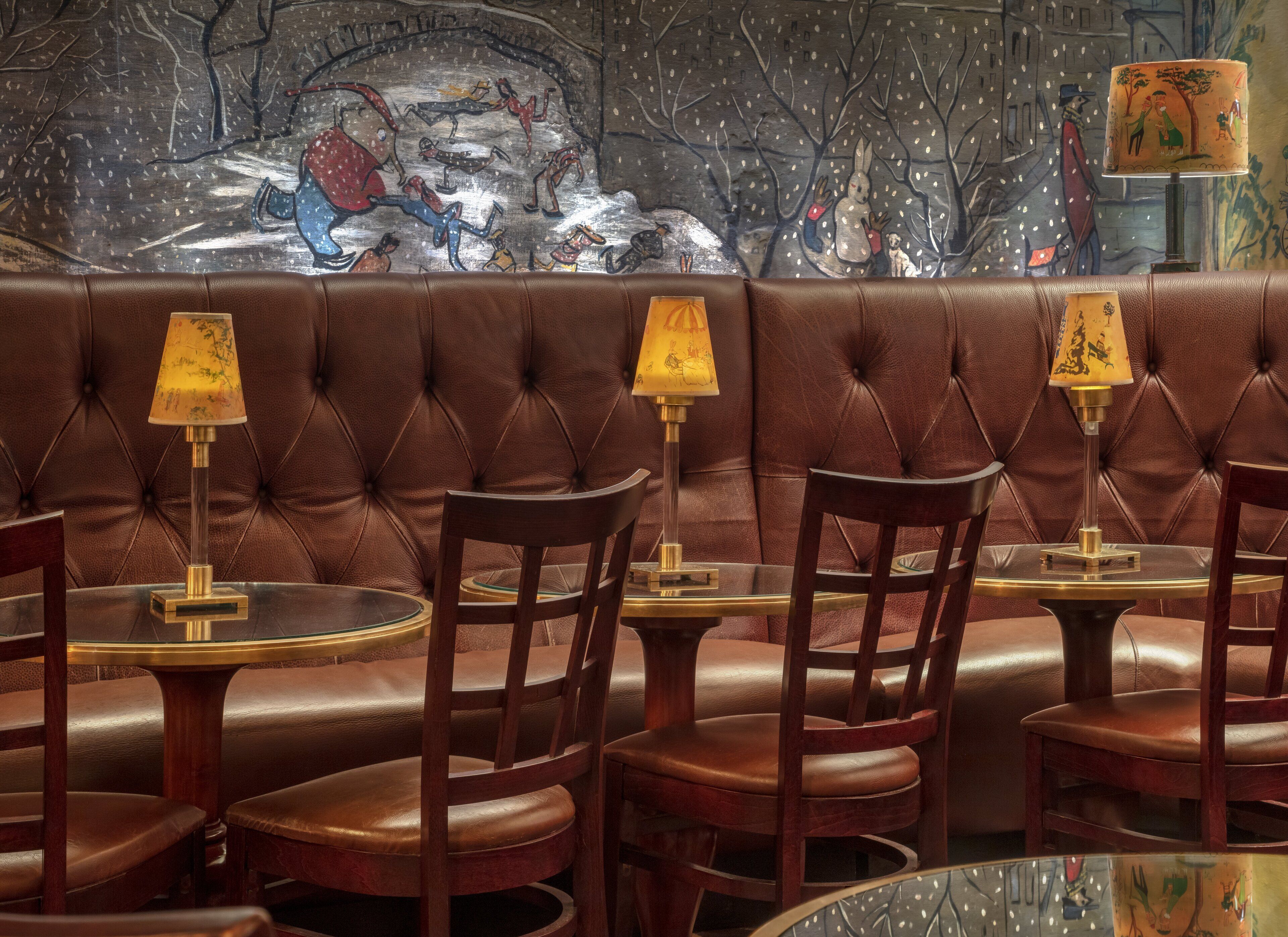 Ein Restaurant mit Ledersitzbänken, runden Tischen und Lampen mit gemusterten Lampenschirmen.