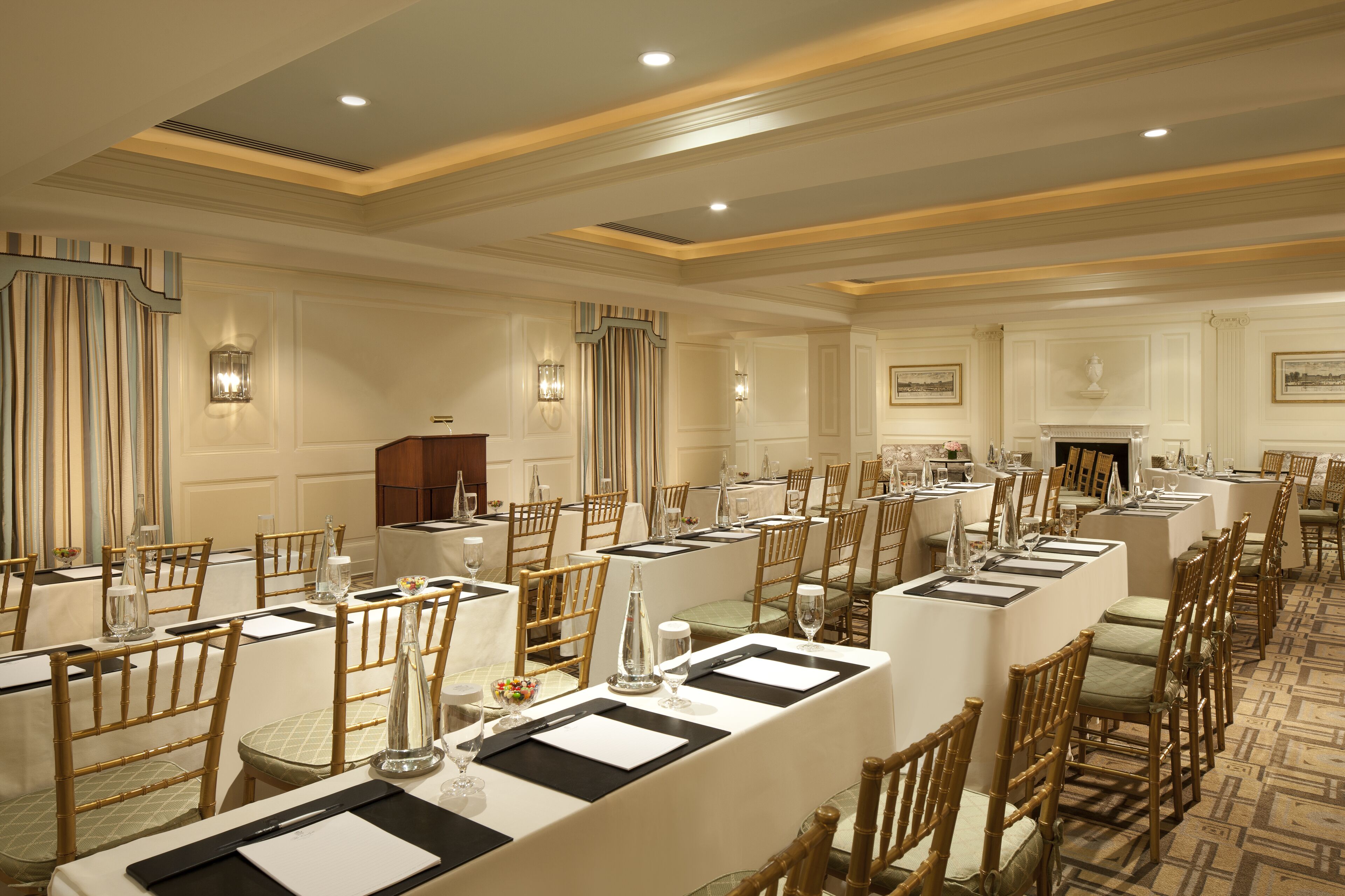 A formal dining room with long tables, wooden chairs, and chandeliers.