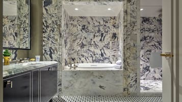 Une salle de bain moderne avec un mur en marbre, une baignoire et un lavabo doté d’un plan de travail en verre.
