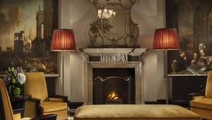 A room with a fireplace, two lamps, a mirror, and a painting. - The Carlyle, A Rosewood Hotel (New York)