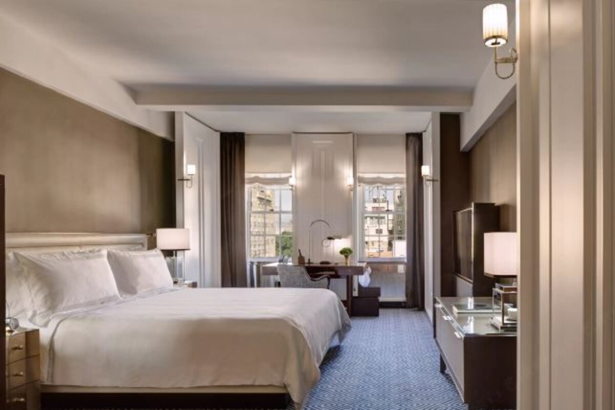 A hotel room with a large bed, a desk with a chair, a TV, and a window with curtains.