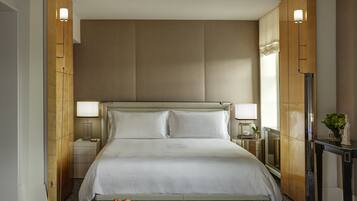 Een hotelkamer met een groot bed, twee bedlampen, een nachtkastje, een klein tafeltje met een vaas en een kamer met een patroon op de vloer.