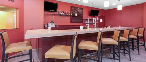 A bar area with a long counter, multiple chairs, and a television mounted on the wall.