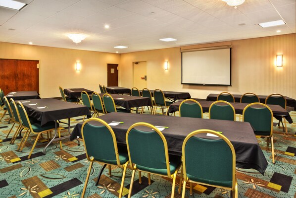 A conference room with multiple tables and chairs, a projector screen, and a carpeted floor.