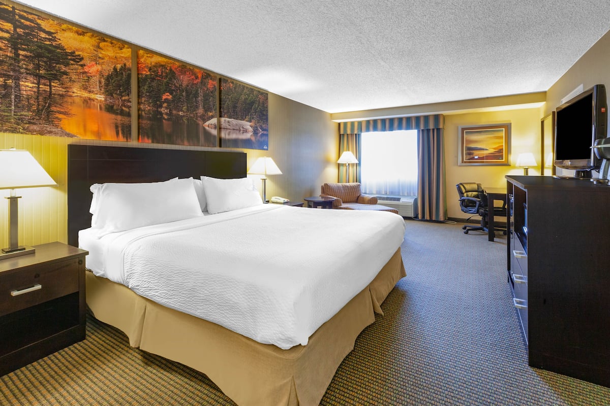 A hotel room with a large bed, two bedside tables, a desk, a chair, a TV, and a painting on the wall.