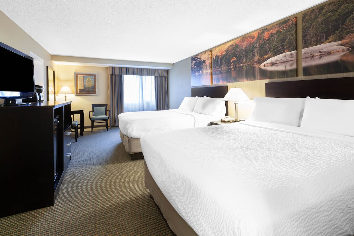 A hotel room with two beds, a desk, a television, and a painting of a lake.