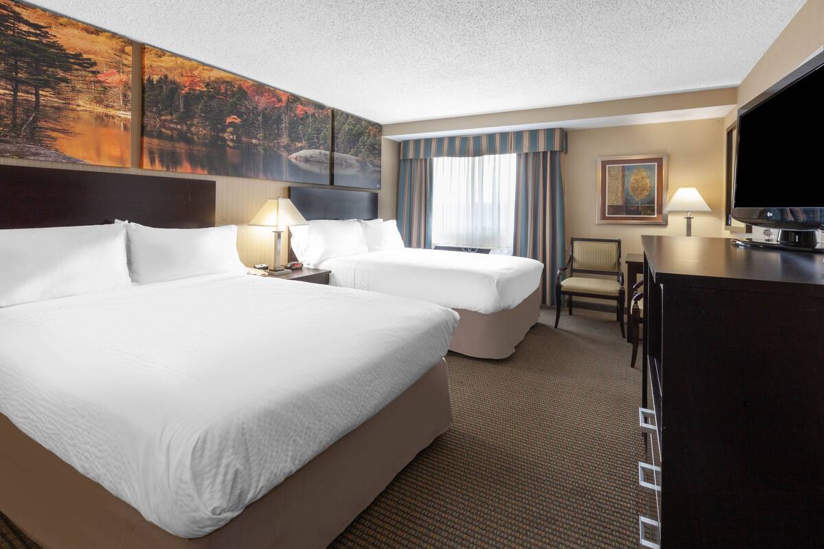 A hotel room with two beds, a desk, a TV, and artwork on the walls.