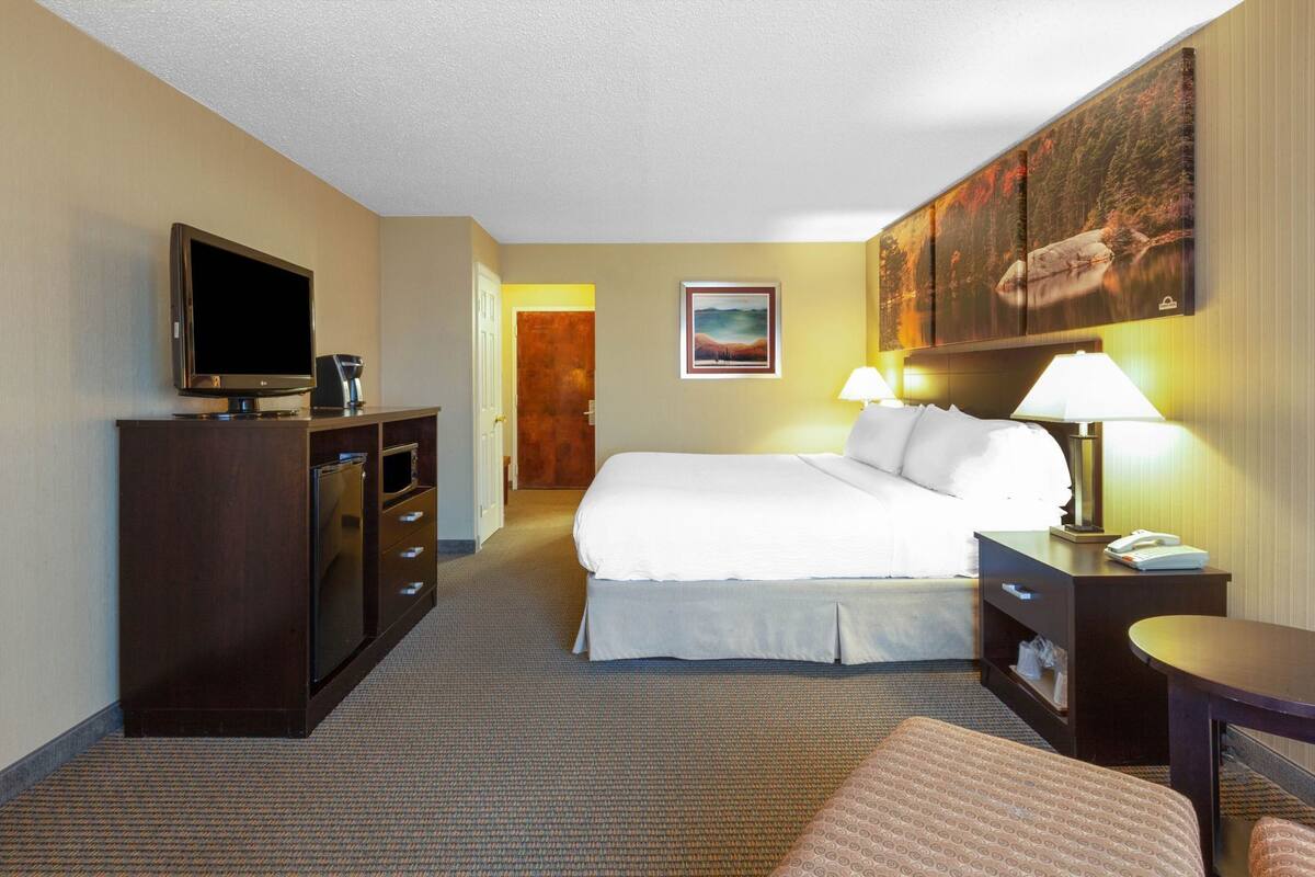 A hotel room with a bed, a desk with a lamp, a TV, and a dresser.