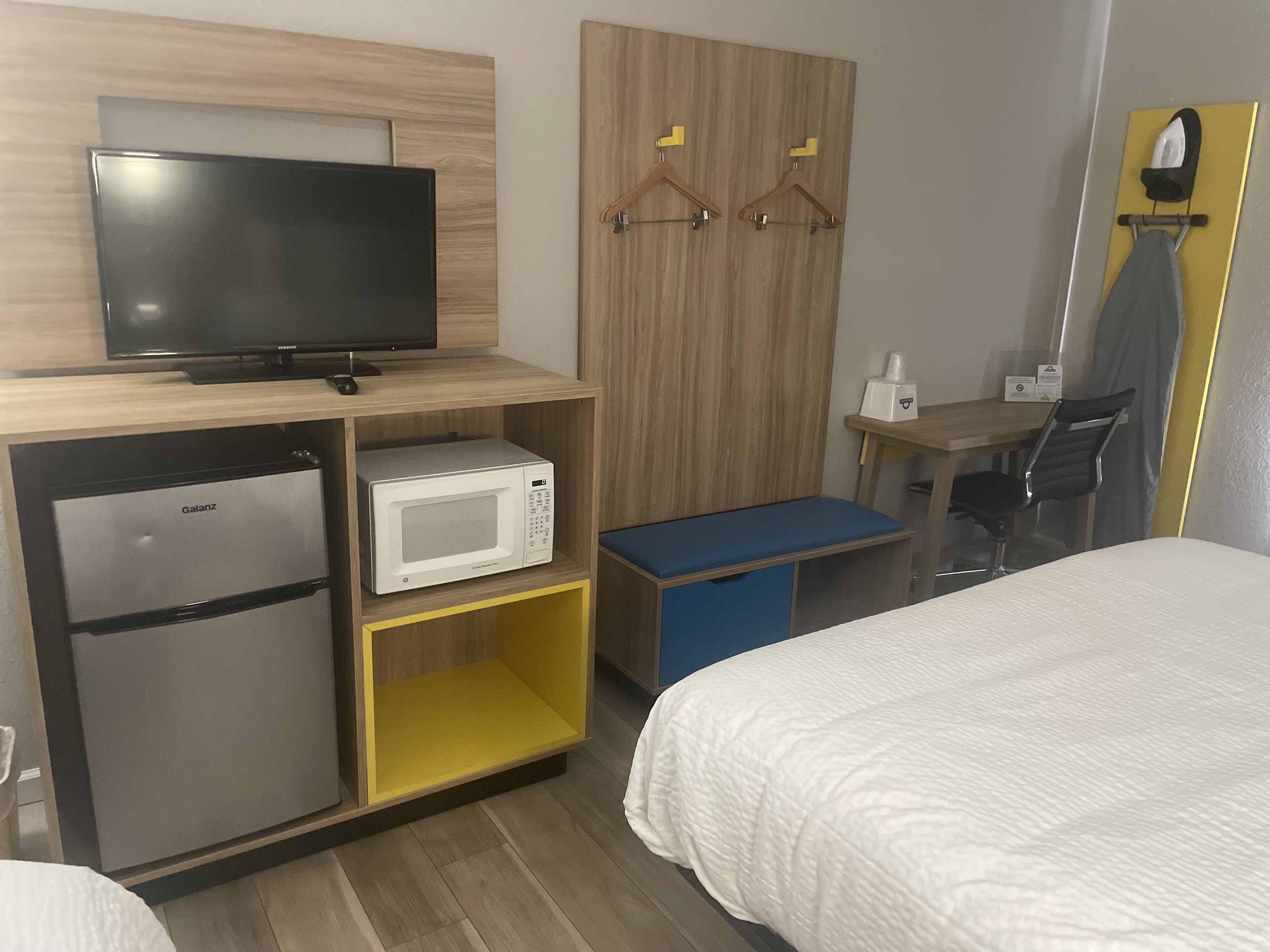 Een hotelkamer met een flatscreen televisie, een magnetron, een minibar, een bureau met stoel en een bed.