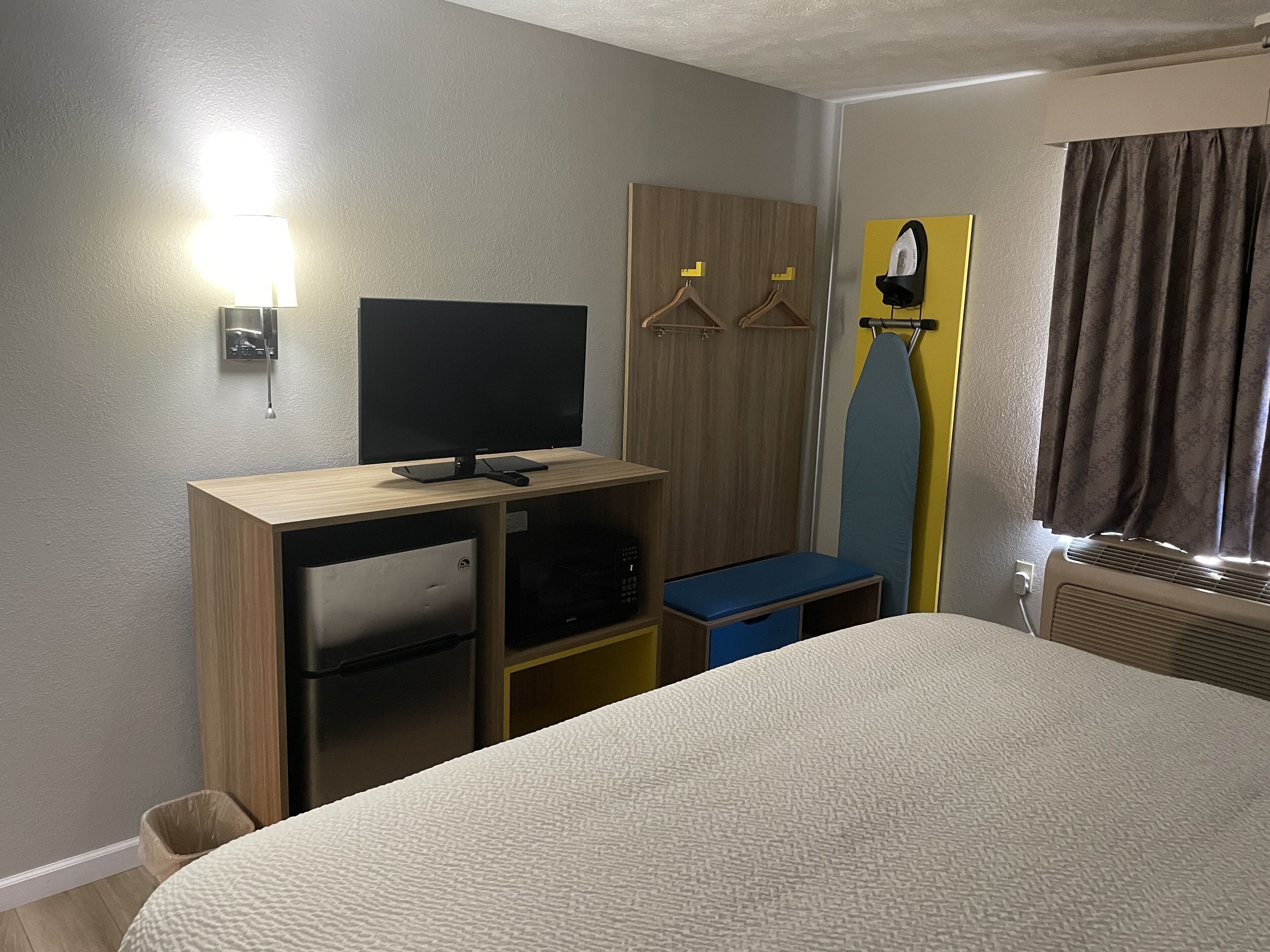 Une chambre d’hôtel comprenant un lit, un bureau avec une télévision, une armoire et une planche à repasser.