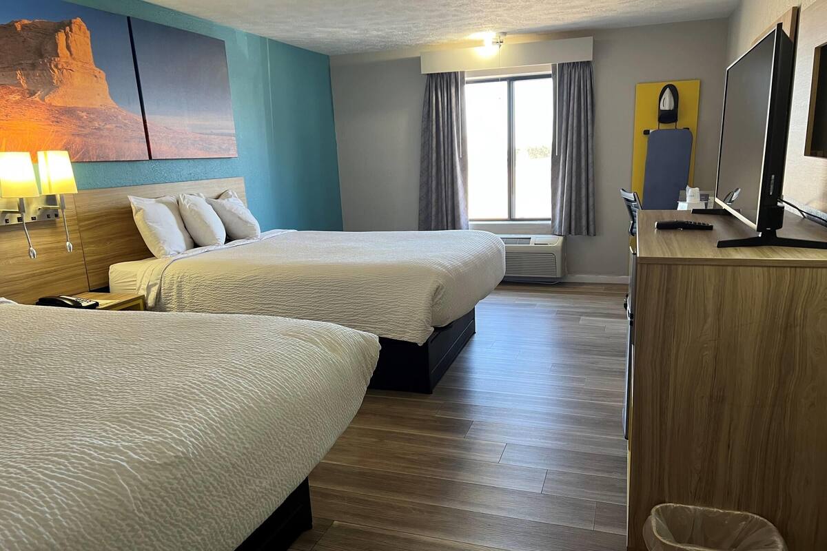A hotel room with two beds, a desk with a computer, a TV, and a large window with curtains.
