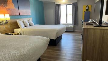 Une chambre d’hôtel avec deux lits, un bureau avec un ordinateur, une télévision et une grande fenêtre avec des rideaux.
