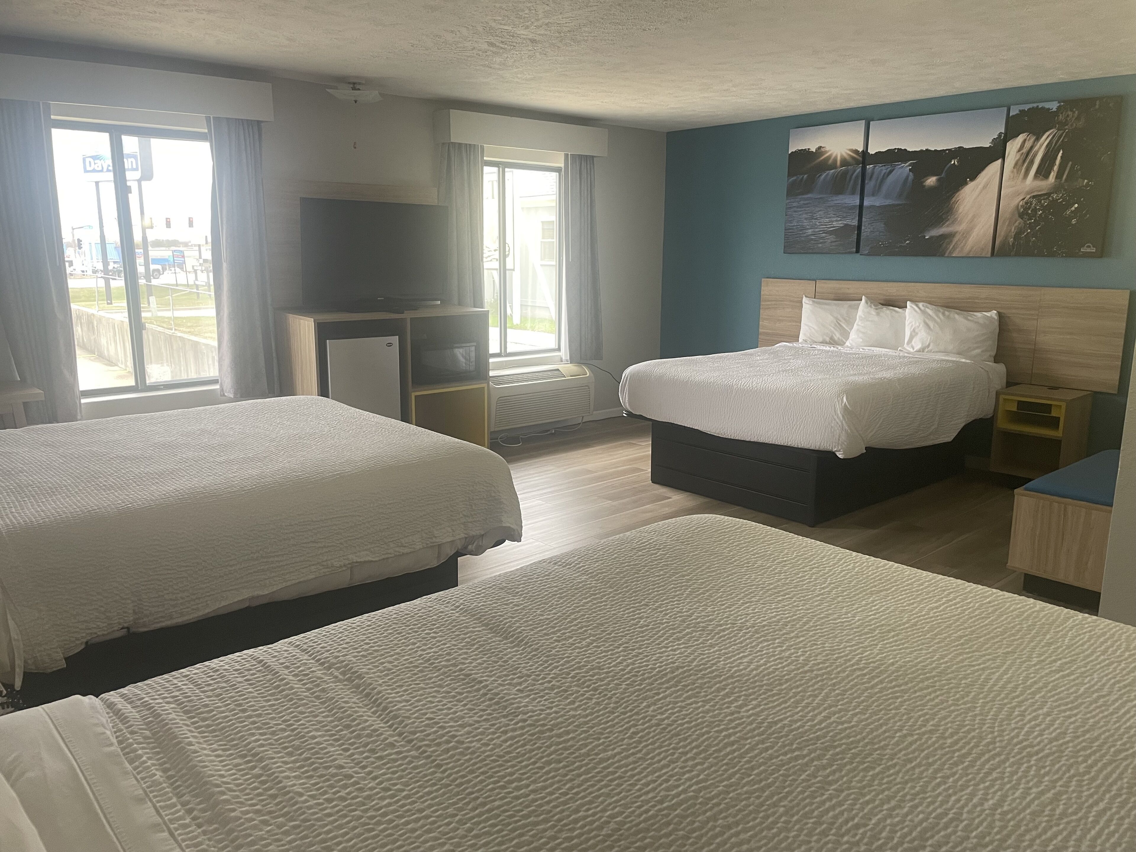 A hotel room with two beds, a TV, a heater, and a large window with a view of the outside.