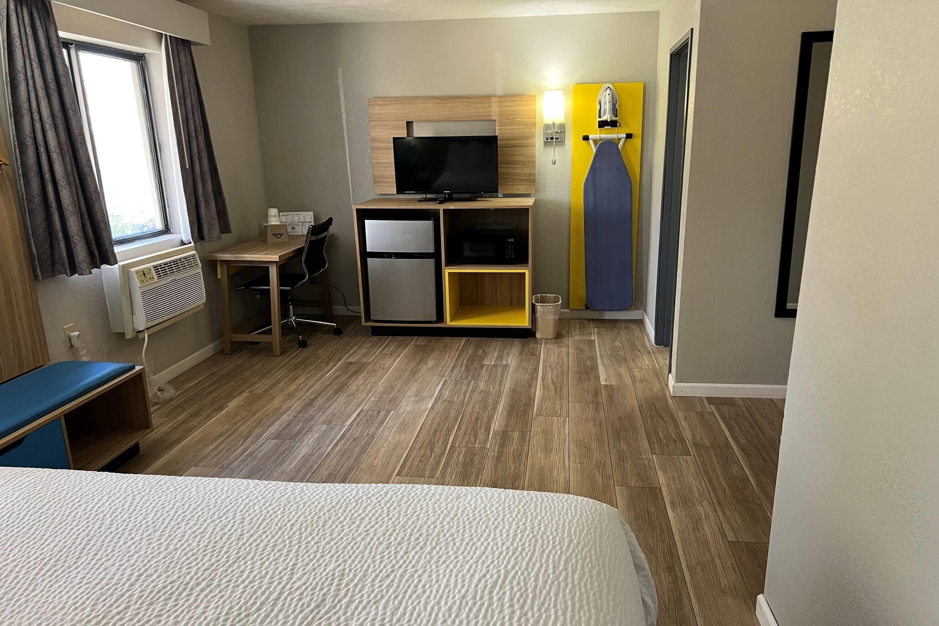 A hotel room with a bed, a desk with a computer, a television, a microwave, and a small refrigerator.