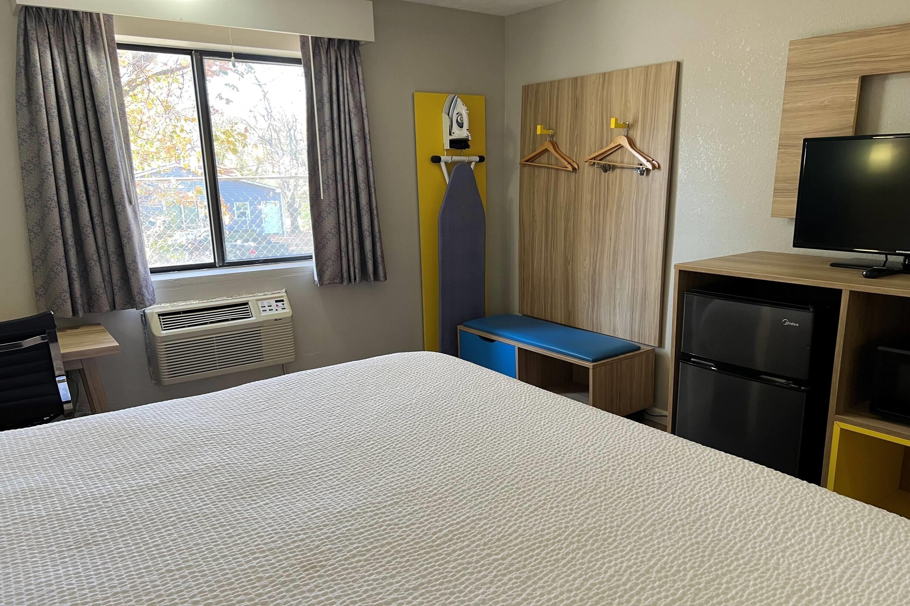 A hotel room with a bed, a desk, a television, a wardrobe, and a window with curtains.