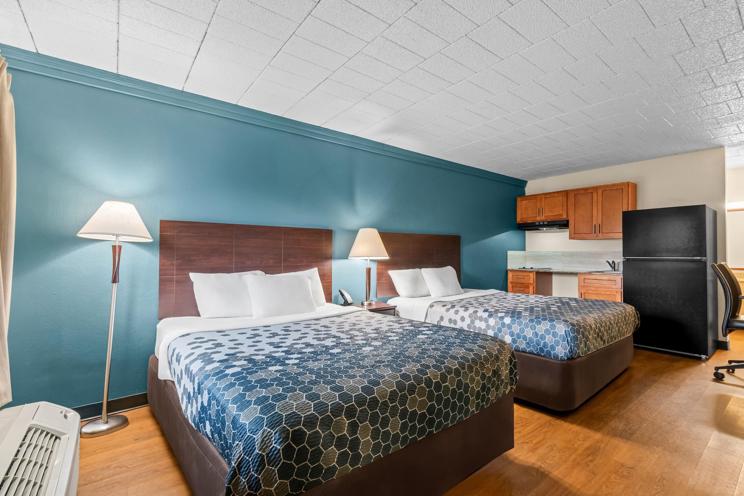 A hotel room with two beds, a kitchenette, and a ceiling fan.