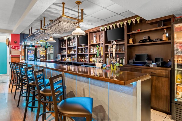 A bar area with a long counter, multiple stools, and a variety of bottles and glasses on shelves. - Travelodge by Wyndham Shamokin Dam/Selinsgrove (Shamokin Dam)